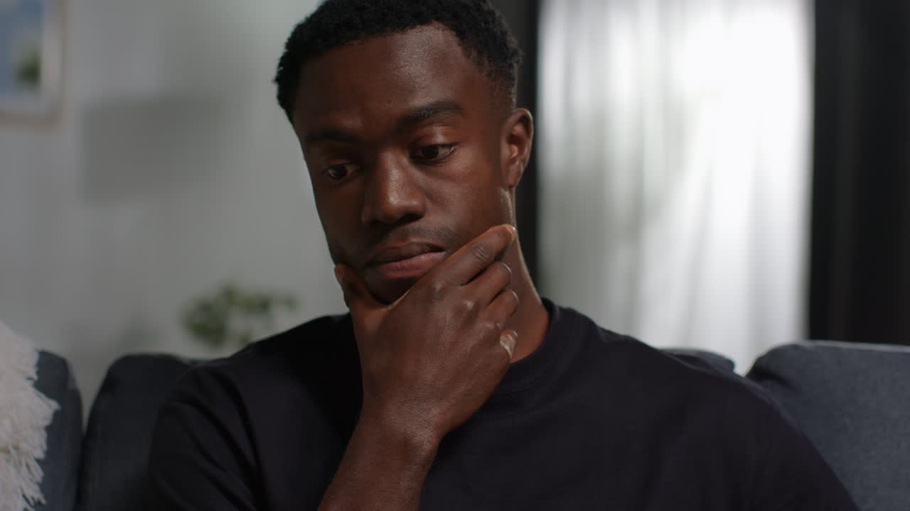 Close Up Of Unhappy And Depressed Young Man Sitting On Sofa At Home Looking Anxious And Worried Resting Head On Hand