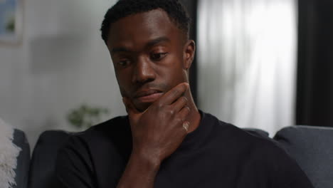 close up of unhappy and depressed young man sitting on sofa at home looking anxious and worried resting head on hand