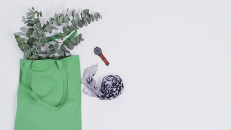 video de una bolsa de lienzo verde con planta, bufanda, reloj, espacio de copia sobre fondo blanco