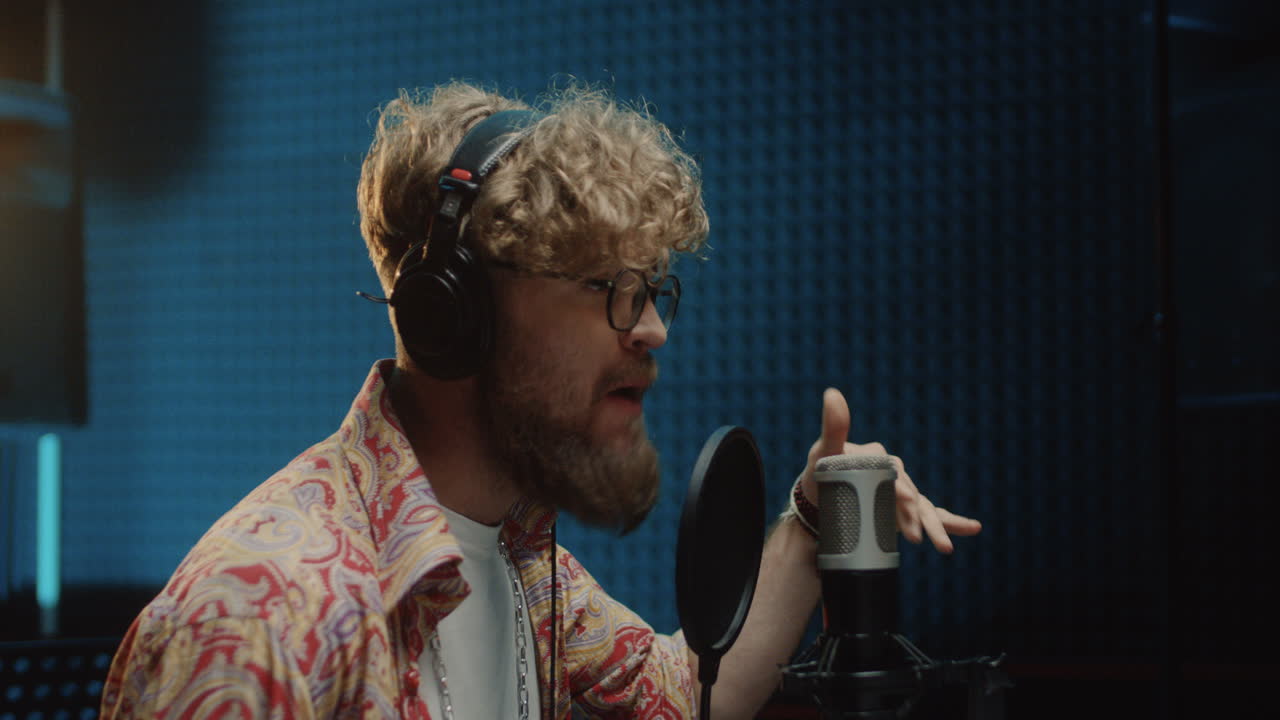 남자 젊은 가수가 마이크에 대고 감정적으로 노래하는 동안 노래와 보컬 부분을 녹음하는 과정