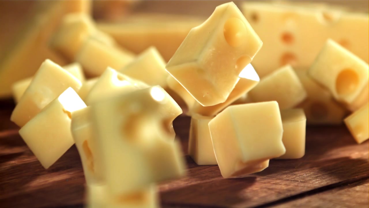 Deliziosi cubetti di formaggio che cadono al rallentatore su un tagliere di legno