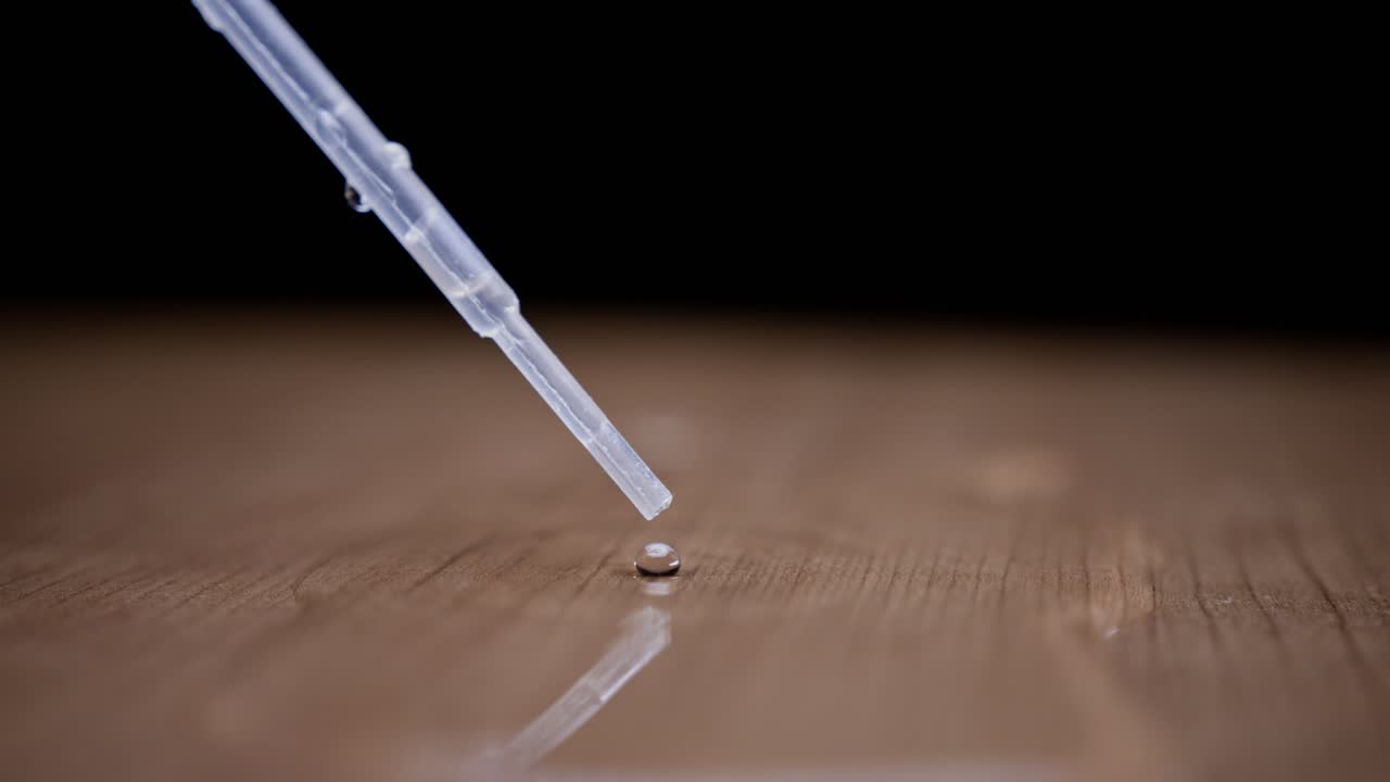 Water droplet from a pipette falling on a smooth surface with a reflective shine