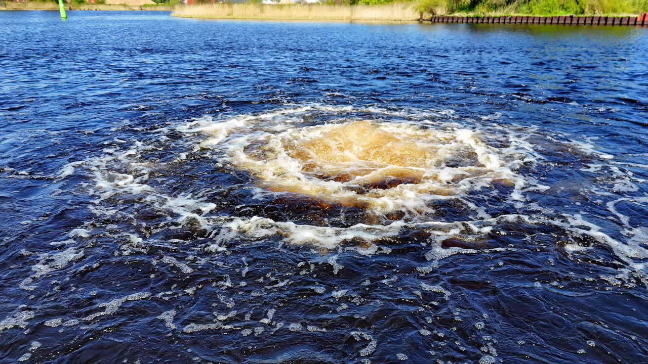 Dynamic Close-Up from the Water's Edge, Capturing the Epicenter of a Powerful Marine Disturbance with a Concentrated Effervescence of Golden-Brown Liquid and Spiraling White Foam Dark Watery Expanse