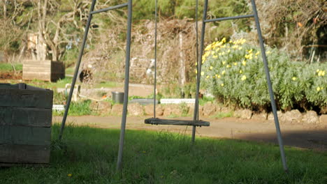 empty old style metal swing with wooden seat moving gently