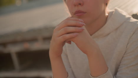 두 손을 함께 고, 은 손을 볼 수 있고, 평온하고 반사적인 분위기를 발산하는 사려 깊은 여성의 클로즈업, 빛이 그녀의 뒤에 부드럽게 빛납니다.