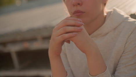 close-up of thoughtful woman with hands locked together, polished nails visible, exuding a calm and reflective mood, sunlight softly glows behind her