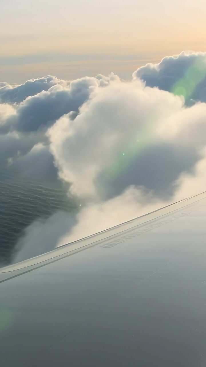 縦型動画：飛行中に積雲の上を降下する航空機の翼が、海を現す様子