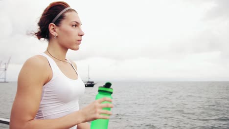 Durstige-Fitnessfrau,-Die-Sich-Nach-Dem-Training-Ausruht-Und-Eine-Wasserflasche-Trinkt.-Schöne-Frau-Beim-Training-Am-Meer