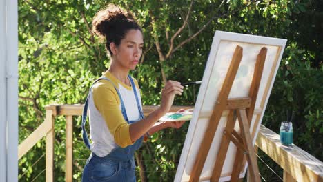 mixed race woman painting on canvas in the balcony at home