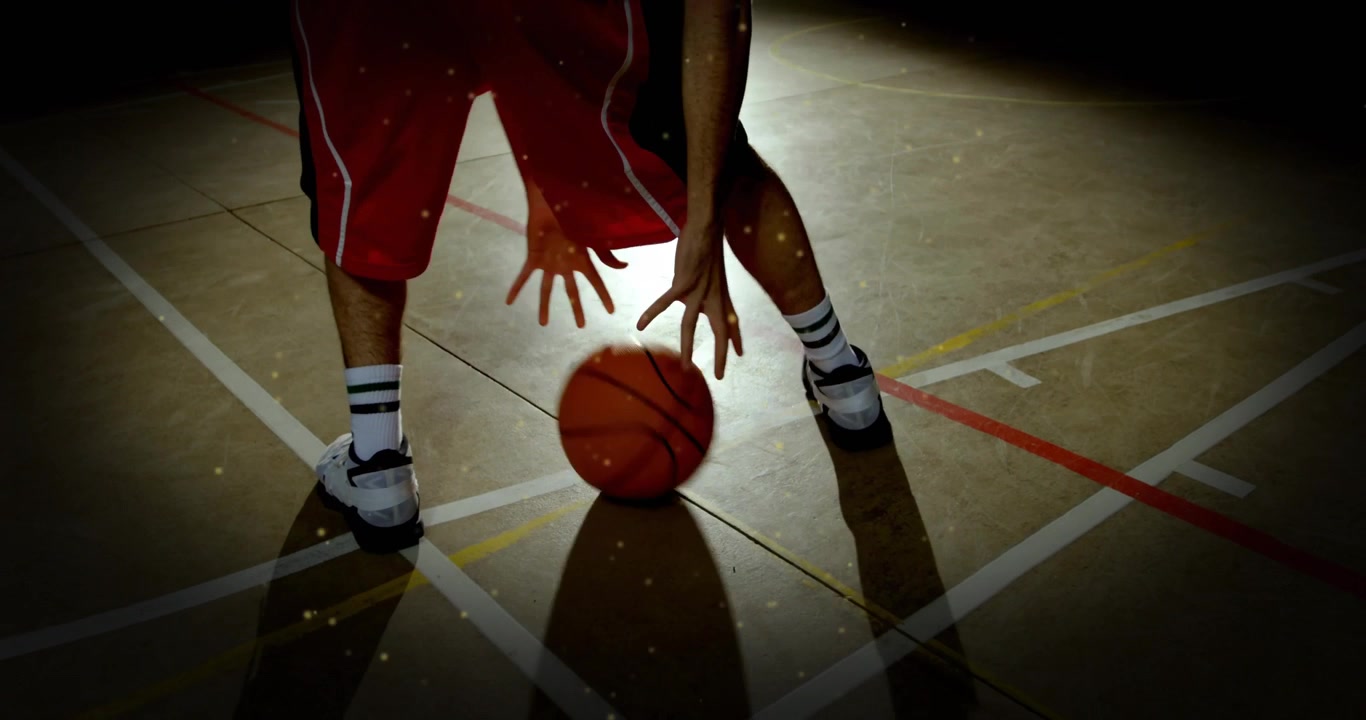 Atleta che inizia un esercizio di palleggio con le gambe, illuminato da un riflettore, mostrando il controllo con la punta delle dita per l'allenamento di pallacanestro.