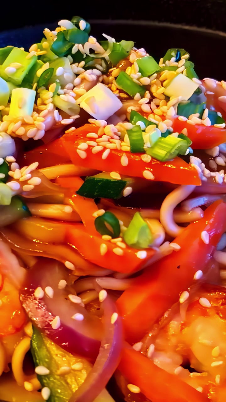 Primo piano estremo di una vivace ciotola di noodle asiatici ricca di udon, peperoni rossi, carote e semi di sesamo, che cattura il colore e la consistenza del cibo da strada asiatico.