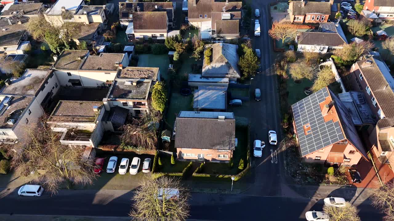 Single family houses with solar panels on roof during golden sunrise in small town of USA. Green garden and Laufes trees in winter. Parking cars on street. Suburb neighborhood of german town. Aerial.