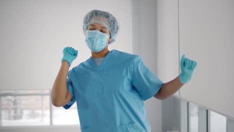 young african american woman wearing scrubs uniform, gloves and mask dancing in hallway