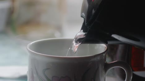 slow motion shot of water pouring from an electric kettle into a coffee cup