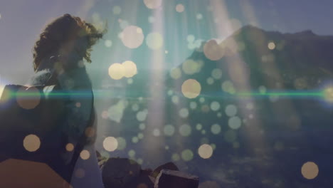 woman standing on rocky shoreline, tech overlay showing lens flare and bokeh effects