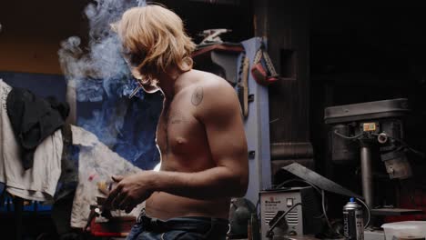 cinematic shot of mechanic with tattoos lighting up a cigarette leaning against his workbench