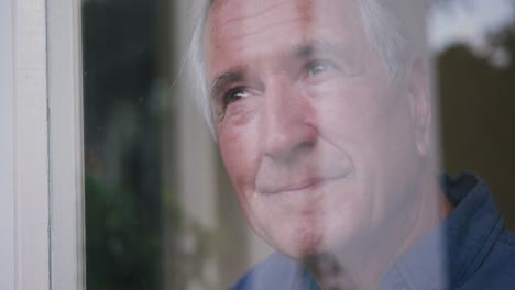 hombre caucásico mayor sonriendo y mirando por la ventana en casa