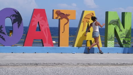 long hair latina runs slo mo along roatan sign on island waterfront