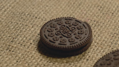 dark brown chocolate cream cookie or biscuit rolling and falling on jute gunny cloth, 4k , stable shot