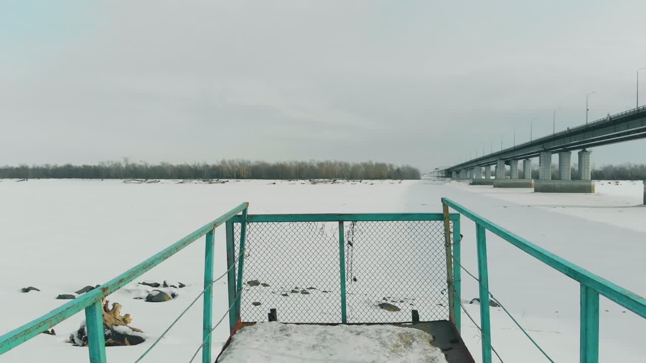 muelle cerrado con rejilla metálica dañada contra el río congelado