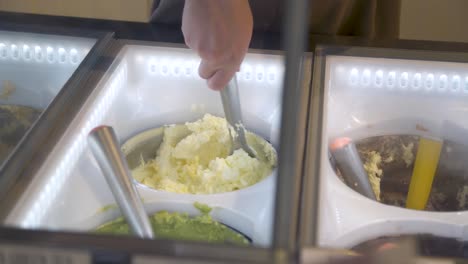 Hand-scooped-vanilla-ice-cream-served-display-freezer-in-yellow-cup