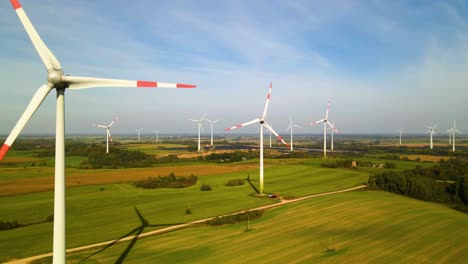 drohnenaufnahme der windkraftanlagen in einem windpark, die an einem sonnigen tag auf einem weiten grünen feld grüne elektrizität erzeugen, nutzung erneuerbarer energiequellen, aufstieg