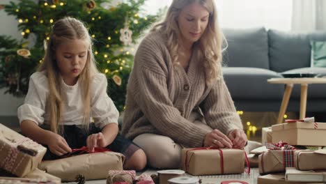 caucasian girl and mother wrapping christmas gifts on the floor.