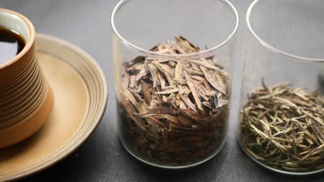diferentes tipos de té de hojas sueltas en recipientes de vidrio y una taza