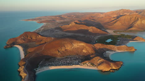 Cinematic-wide-revealing-drone-shot-of-Balandra-Beach,-view-of-red-hills,-turquoise-waters,-white-sand-beaches,-and-mountains-during-sunset