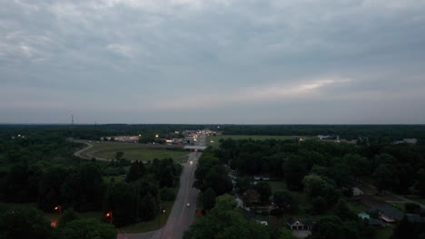 aerial drone forward moving shot over highway running through small town with cars passing by during evening time