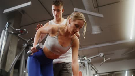 mujer levantando pesas con entrenador personal en el gimnasio