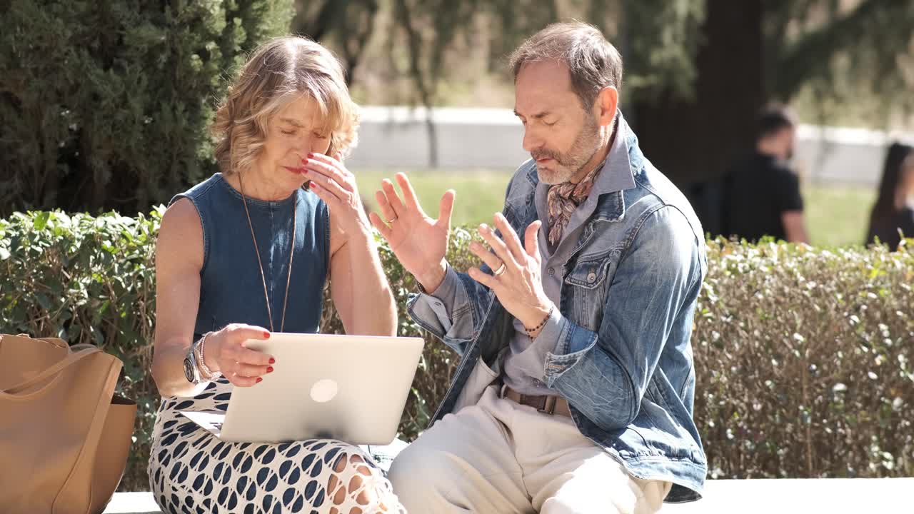Frustrated mature couple using netbook in park receiving bad news