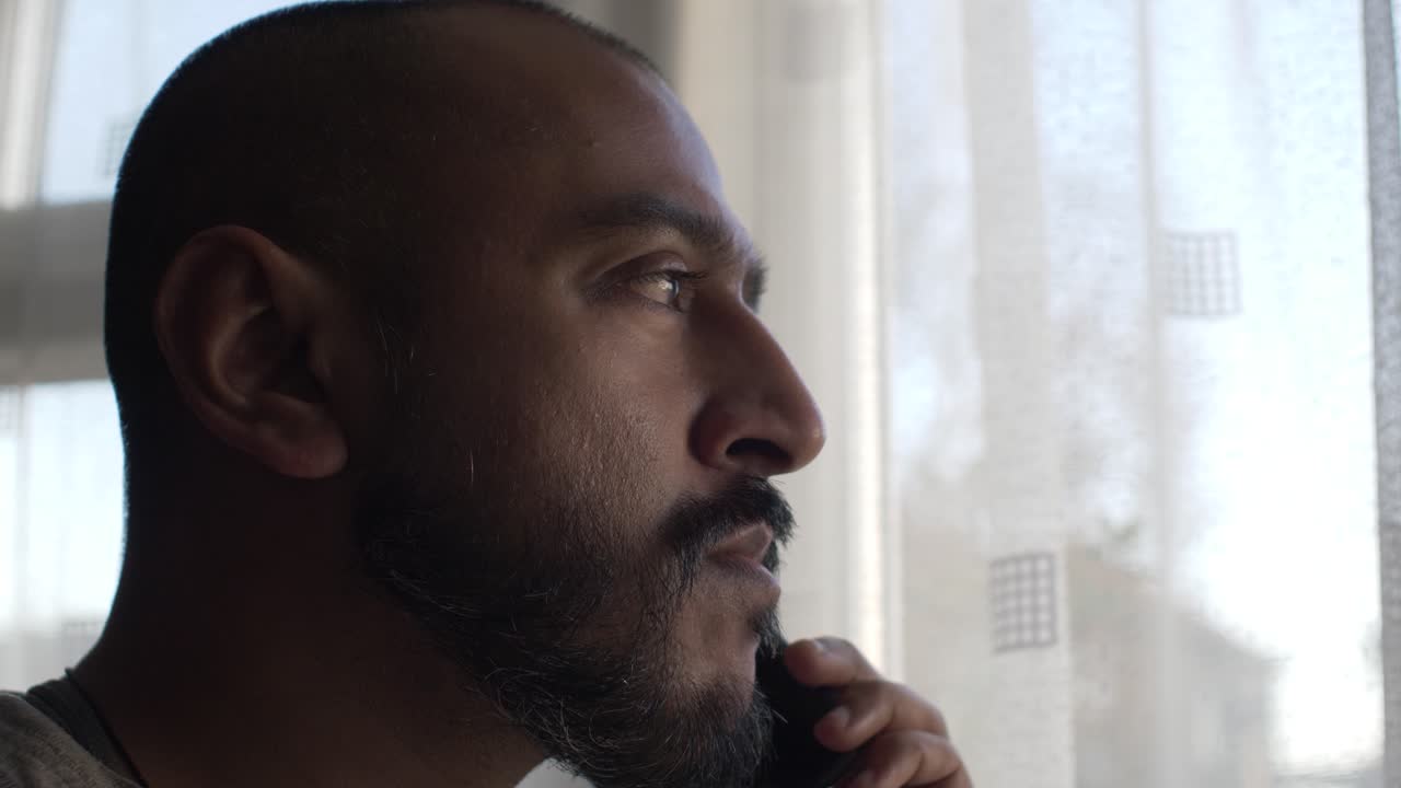 Adult Asian Male Indoors On Mobile Phone Looking Through Curtain