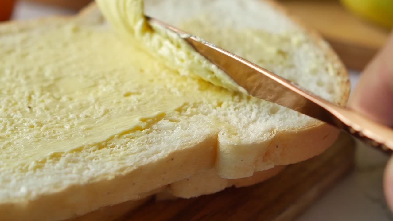 Mantequilla fresca en un recipiente con pan sobre fondo blanco.