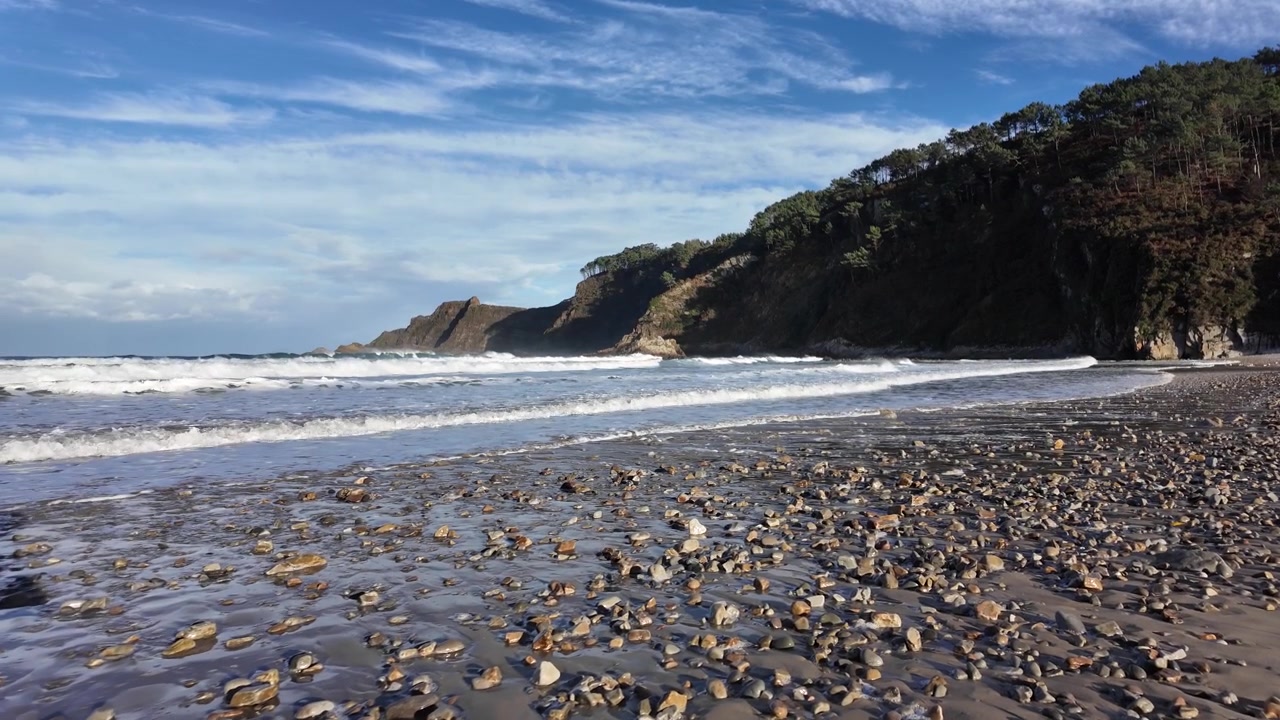 Ondas quebrando em uma praia de seixos com areia molhada texturizada em primeiro plano.