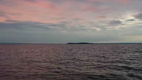 Cinematic-Drone-aerial-flying-over-the-water-revealing-pink-sunset