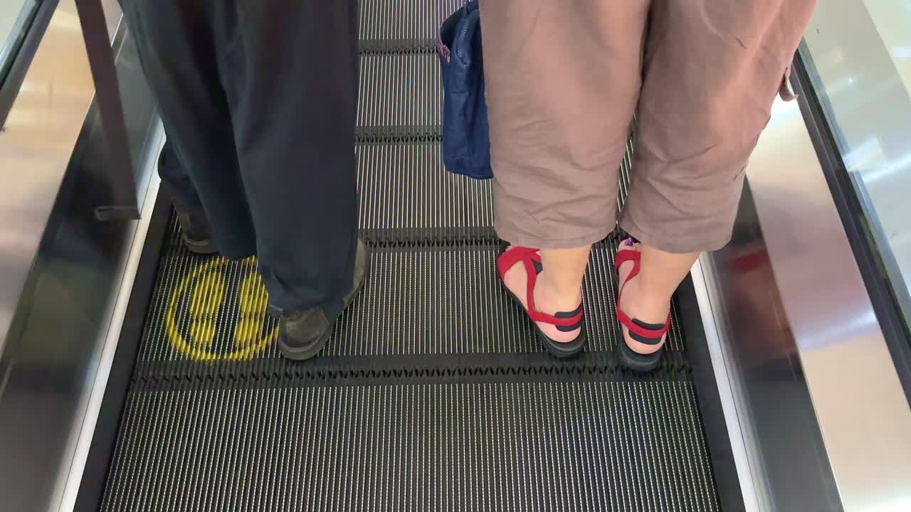 Feet on the escalator with yellow foot marks. Yellow standing signs on the escalator.