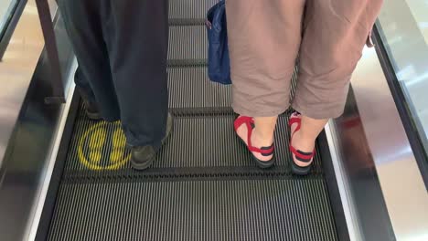 feet on the escalator with yellow foot marks. yellow standing signs on the escalator.