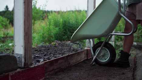 man with wheelbarrow pouring soil and leveling ground using rake tool