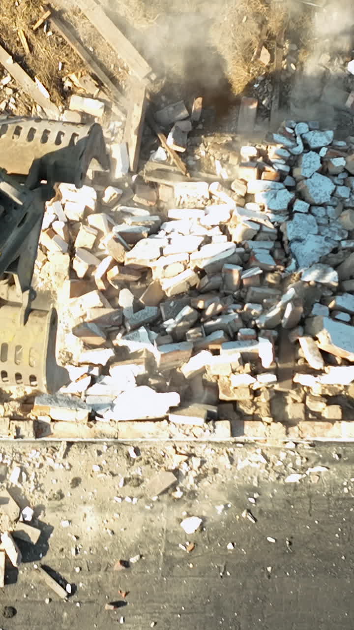 A powerful hydraulic excavator claw smashes through a brick wall, creating debris and dust in a cinematic topdown construction scene