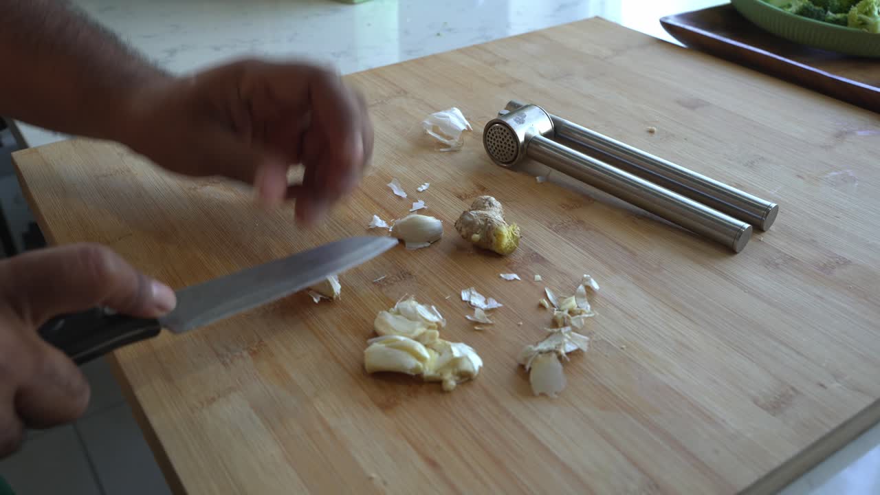 Hands peeling garlic and ginger on a cutting board