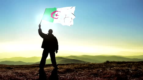 exitoso hombre silueta ganador agitando la bandera de argelia en la parte superior del pico de la montaña. fondo de bucle cinemagraph