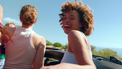 Female-Friends-Standing-Up-Through-Sun-Roof-Of-Car-On-Road-Trip-Through-Countryside