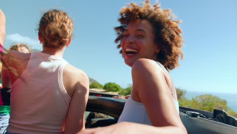 female friends standing up through sun roof of car on road trip through countryside