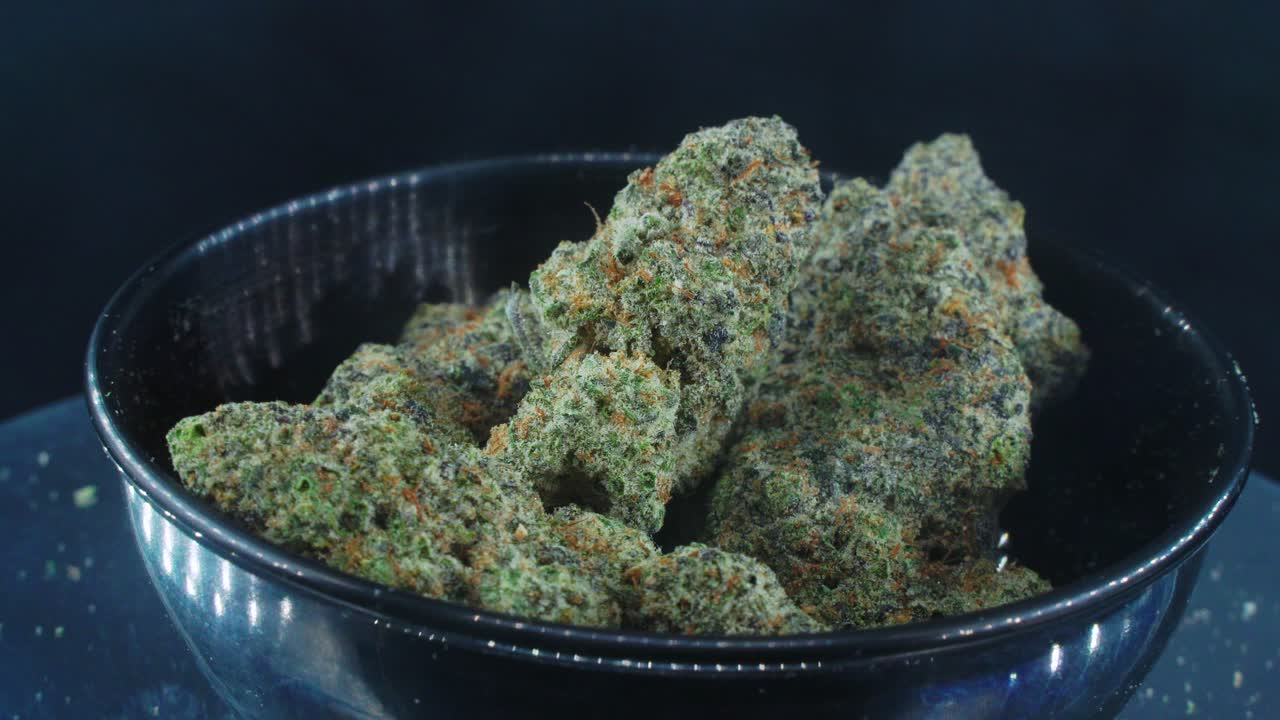 Green Dried Marijuana Buds Close Up concept Shot, pile of dried marijuana plants, orange trichomes strains, in small black shiny bawl, on a rotating stand, studio lights, slow motion, 4K video, smoke