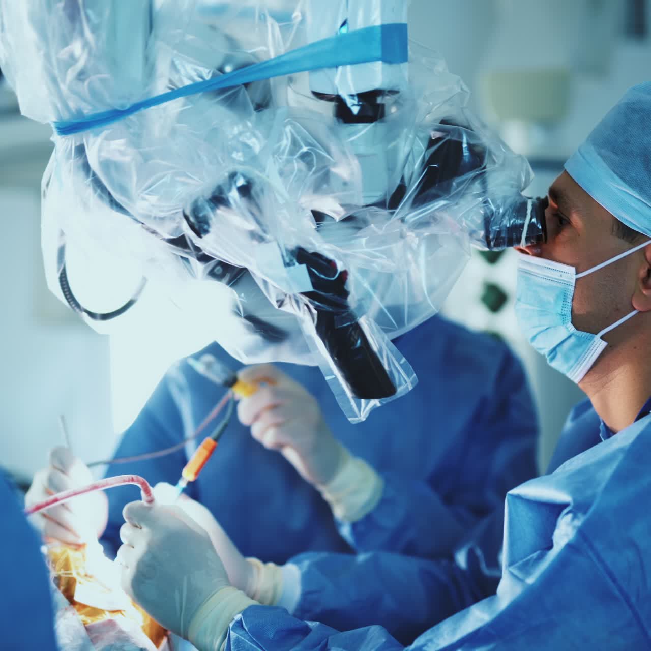 Team of surgeons working hard at surgery room. Experienced doctors use diverse tool and advanced powerful microscope at operation. Blurred backdrop