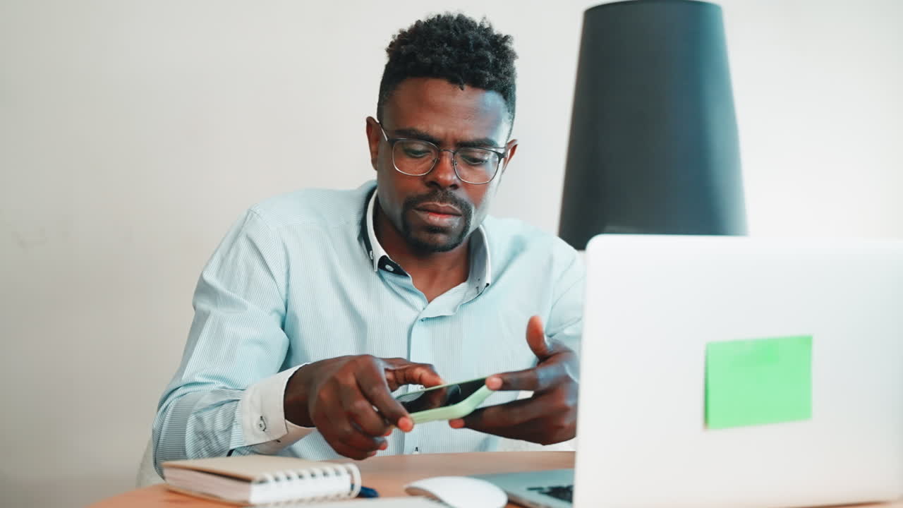 Uomo che lavora al laptop e tiene in mano il telefono