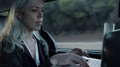 gray haired woman in suit typing on laptop in car