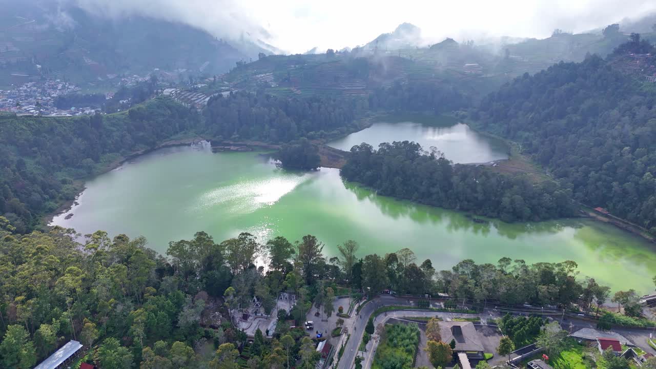 Beautiful drone footage of a crater lake with greenish water nestled among forested hills and cloudy mountains. Tranquil and picturesque highland scenery captured from above
