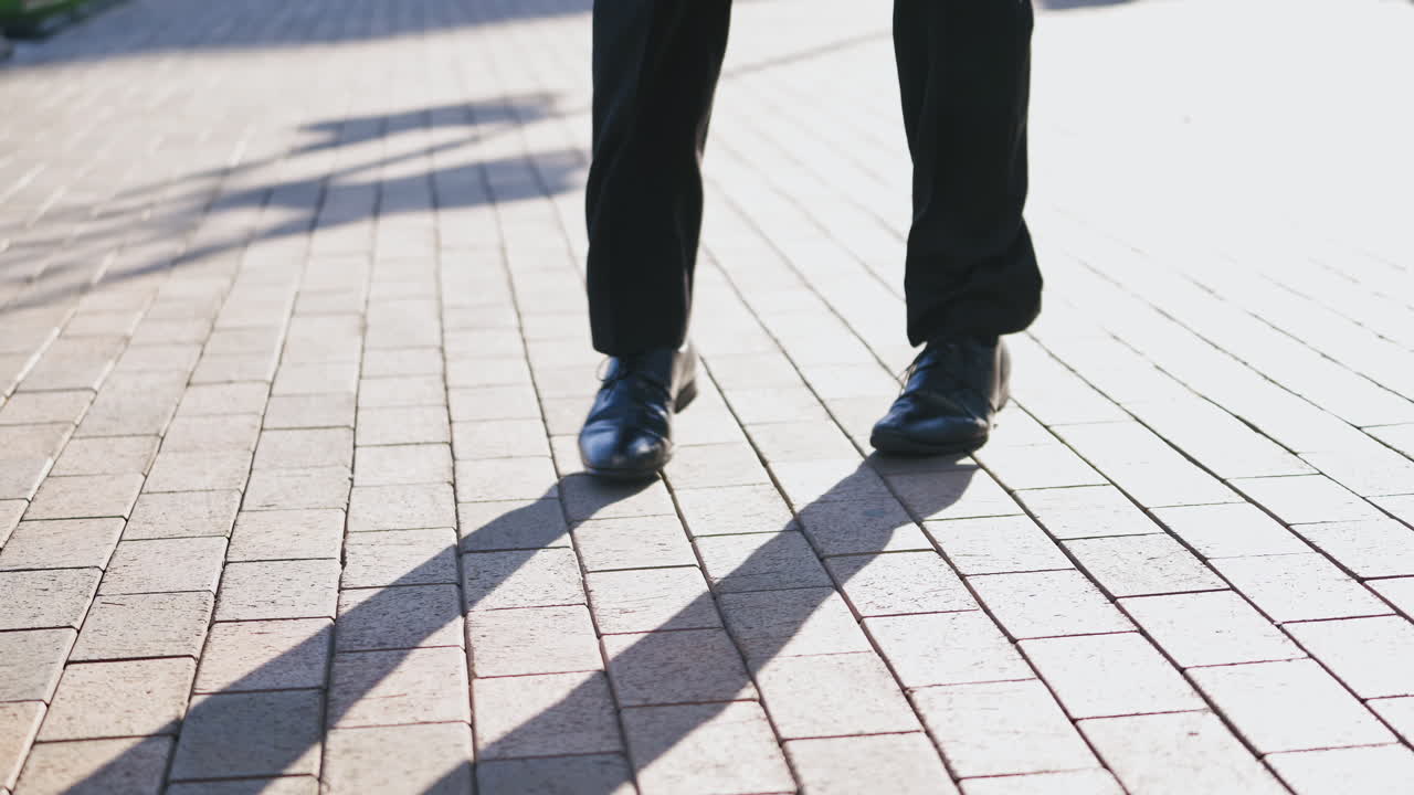Close-up for legs of man in black shoes dancing in the street. Male's feet in black shoes and trousers dances happily on the pavement outdoors.